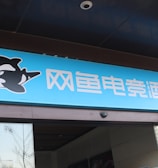 A building entrance features a vibrant blue sign with white Chinese characters and a stylized orca logo in black and white. The overall appearance suggests an establishment focused on eSports or digital activities.